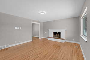 Unfurnished living room featuring light wood-type flooring, a brick fireplace, visible vents, and baseboards