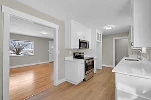 Kitchen featuring white cabinets, light wood finished floors, stainless steel appliances, and a sink