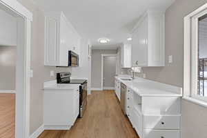 Kitchen featuring stainless steel appliances, white cabinetry, a sink, and light wood-style flooring