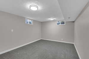 Below grade area featuring visible vents, dark carpet, a textured ceiling, and baseboards