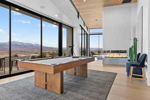 Recreation room with wood ceiling, a wall of windows, wood finished floors, and a mountain view