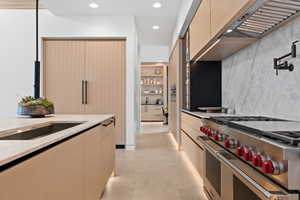 Kitchen with range with two ovens, recessed lighting, light brown cabinets, modern cabinets, and wall chimney exhaust hood