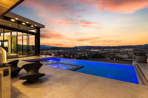 Pool at dusk featuring an infinity pool, a patio area, a mountain view, and an in ground hot tub