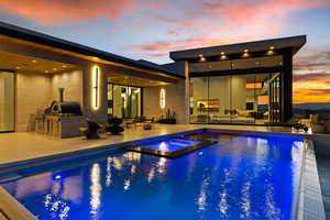 Pool at dusk featuring an outdoor hangout area, a grill, exterior kitchen, a patio area, and a pool with connected hot tub