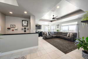 Living area with a tray ceiling, light tile patterned floors, recessed lighting, a ceiling fan, and baseboards