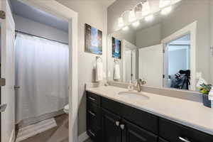 Bathroom with toilet, a shower with shower curtain, and vanity