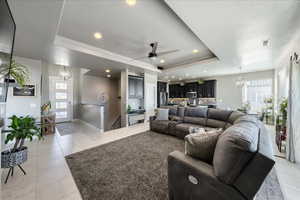 Living area featuring light tile patterned floors, baseboards, visible vents, a raised ceiling, and ceiling fan with notable chandelier