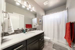 Bathroom featuring shower / bath combination with curtain, visible vents, backsplash, toilet, and vanity