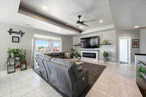 Living room featuring ceiling fan, a glass covered fireplace, a raised ceiling, and visible vents