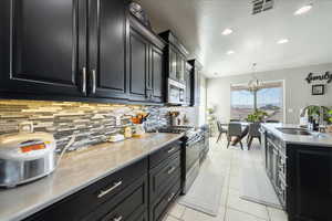 Kitchen with light tile patterned floors, dark cabinets, a sink, visible vents, and appliances with stainless steel finishes