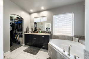 Bathroom featuring tile patterned flooring, a spacious closet, a bath, and double vanity