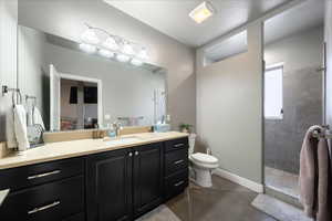 Full bathroom featuring toilet, vanity, tiled shower, concrete floors, and baseboards