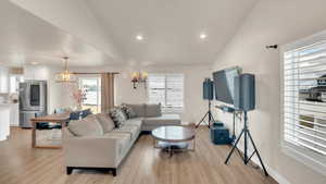 Living room with light wood-type flooring, lofted ceiling, sink, and an inviting chandelier