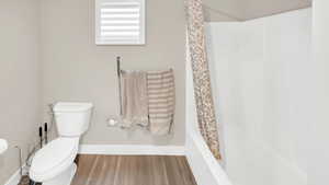 Bathroom with hardwood / wood-style flooring, shower / bath combination with curtain, and toilet