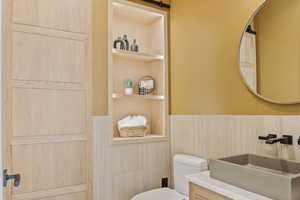 Bathroom with built in features, wainscoting, a sink, and toilet