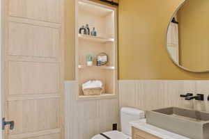 Bathroom with a wainscoted wall, built in shelves, a sink, and toilet