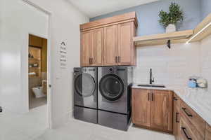 Washroom with cabinet space, light tile patterned flooring, a sink, and washing machine and clothes dryer