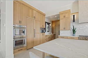 Kitchen featuring appliances with stainless steel finishes, light stone countertops, decorative backsplash, and light brown cabinetry