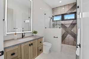 Bathroom featuring toilet, a tile shower, and vanity