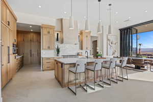 Kitchen with black oven, light countertops, hanging light fixtures, wall chimney exhaust hood, and a large island with sink