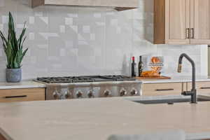 Kitchen featuring light countertops, stainless steel gas stovetop, decorative backsplash, and light brown cabinetry