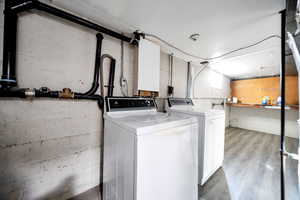 Laundry room with laundry area, wood finished floors, and separate washer and dryer and storage.