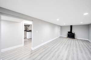 Finished basement with light wood-type flooring, washer / clothes dryer, baseboards, and a wood stove