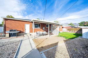 Back of house featuring brick siding, fence, a lawn, and a covered patio