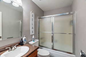 Full bathroom with a textured ceiling, bath / shower combo with glass door, vanity, and toilet