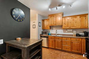 Kitchen featuring dark countertops, appliances with stainless steel finishes, brown cabinets, a textured ceiling, and a sink