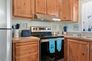 Kitchen with stainless steel appliances, brown cabinets, light countertops, and under cabinet range hood