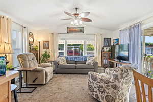 Living room featuring a ceiling fan, lofted ceiling, and carpet flooring