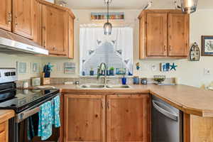 Kitchen featuring decorative light fixtures, light countertops, appliances with stainless steel finishes, a sink, and under cabinet range hood