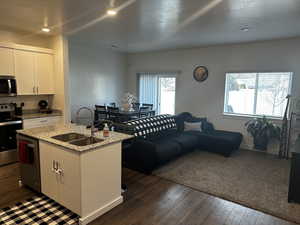 Kitchen with dark wood-type flooring, a sink, appliances with stainless steel finishes, light stone countertops, and a center island with sink