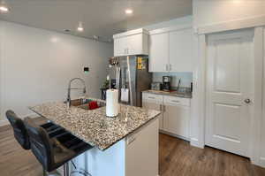 Kitchen with dark wood finished floors, stainless steel fridge with ice dispenser, a kitchen breakfast bar, white cabinetry, and a sink