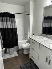 Full bath featuring shower / tub combo with curtain, vanity, toilet, and wood finished floors