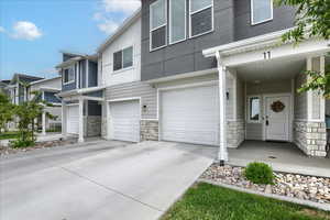 Multi unit property featuring an attached garage, stone siding, and driveway