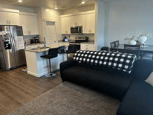 Kitchen with a center island with sink, appliances with stainless steel finishes, dark wood-type flooring, white cabinetry, and a sink