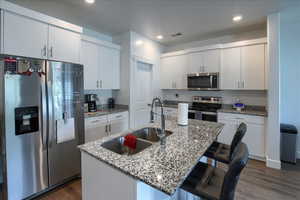 Kitchen featuring dark wood-type flooring, a sink, visible vents, a kitchen breakfast bar, and appliances with stainless steel finishes