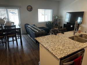 Kitchen with light stone counters, dark wood-style flooring, stainless steel dishwasher, open floor plan, and a sink