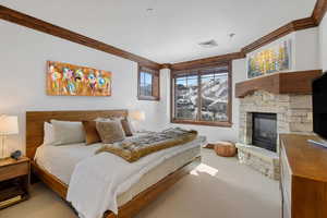 Bedroom featuring ornamental molding, a stone fireplace, carpet, and visible vents