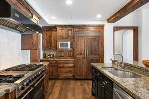 Kitchen with premium appliances, dark wood-style floors, tasteful backsplash, a sink, and wall chimney range hood