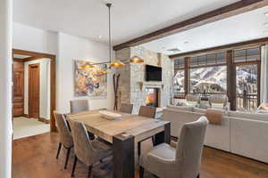 Dining space featuring dark wood-style flooring, a fireplace, visible vents, beamed ceiling, and baseboards