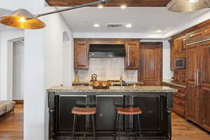 Kitchen with light stone counters, visible vents, stainless steel microwave, wood finished floors, and extractor fan