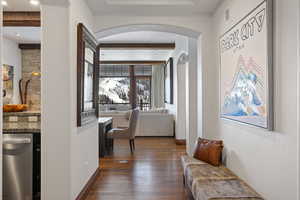 Hallway with arched walkways, visible vents, baseboards, beam ceiling, and dark wood-style floors