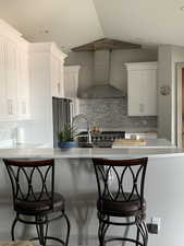 Kitchen with premium appliances, light countertops, white cabinetry, vaulted ceiling, and wall chimney exhaust hood