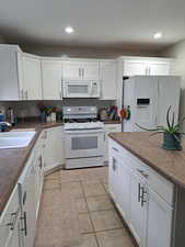 Kitchen with white appliances, dark countertops, a sink, and white cabinetry