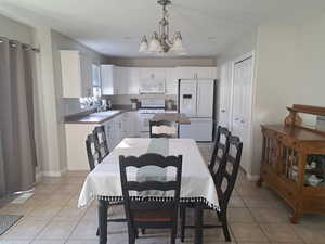 Dining space with baseboards, light tile patterned flooring, and an inviting chandelier