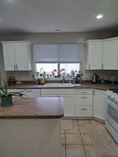 Kitchen with dark countertops, white range with gas stovetop, white cabinetry, and a sink