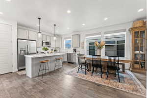 Kitchen featuring light countertops, appliances with stainless steel finishes, a kitchen island, wood finished floors, and a kitchen bar